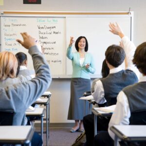 Teacher engaging students with raised hands in classroom.