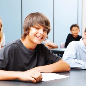 Smiling teenage boy sitting at desk in classroom.