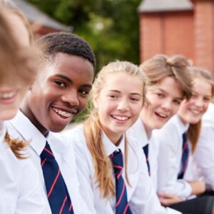 A diverse group of smiling students in school uniforms sitting together outdoors.